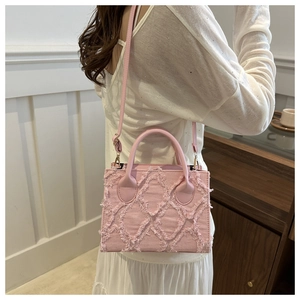 Detail of pink denim tote bag with distressed fringe trim and leather handle on a model