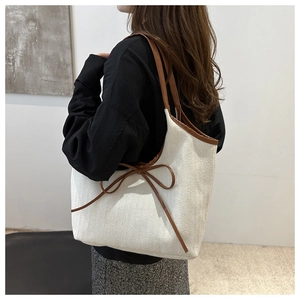 Detail of woven tote bag featuring brown leather handles and a bowknot decoration