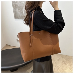 Detail of a large brown leather tote bag with a front pocket and decorative metal strap buckle
