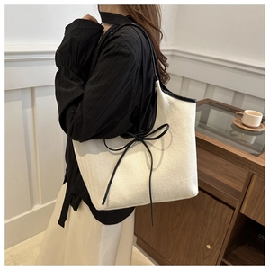 Close-up of off-white canvas tote bag featuring black leather trim and delicate bow detail