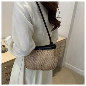 Detail of a straw woven crossbody bag with black leather straps on a female model