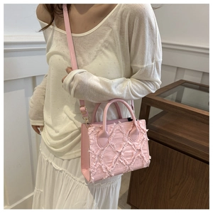 Pink denim crossbody bag with fringe details and quilted pattern on white background