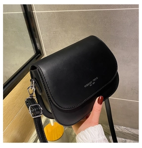 Detail view of black faux leather saddle bag with silver buckle and adjustable strap