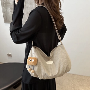 Minimalist beige shoulder tote bag with plush charm shown on a model in a modern interior