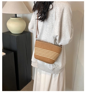 Brown woven straw crossbody bag with white stripes worn by a model in a minimalist room