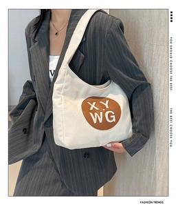 Detail of off-white canvas shoulder bag with brown leather patch on grey blazer