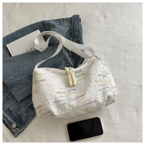 Close-up of white canvas hobo bag with colorful wave embroidery and braided rope knot