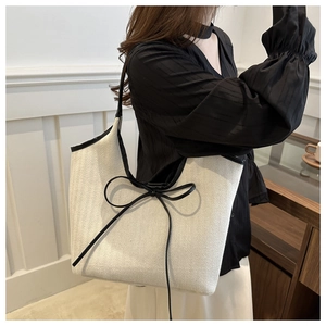 Detail of minimalist cream woven tote bag with black leather trim and bow tie detail