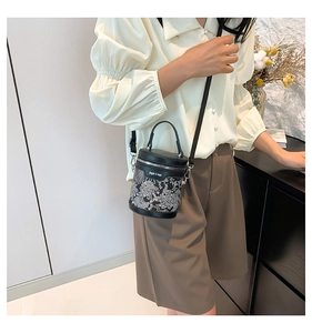 Detail of a black bucket bag with white floral print on a model wearing casual attire
