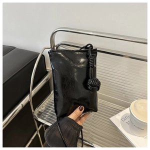 Détail du sac de téléphone noir brillant avec nœud décoratif épais sur la lanière