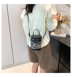 Detailed view of women's black leather bucket bag with dragon embroidery worn crossbody