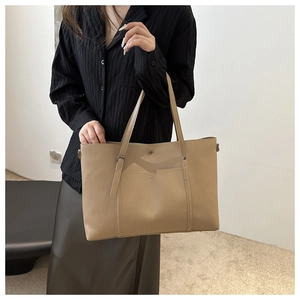 Side view of soft leather tote bag with front pocket shown on a model in a minimalist setting