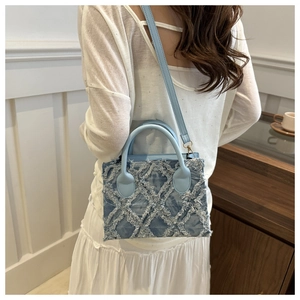 Detailed close-up of light blue denim tote with frayed diamond pattern and leather strap
