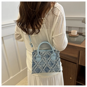 Detail of light blue denim crossbody bag with distressed fringe and quilted texture design