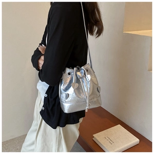 Close-up of silver metallic drawstring bucket bag with heart appliqués and pleated texture