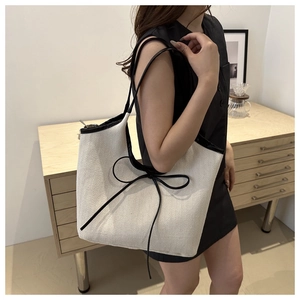 Close-up of cream canvas tote bag with black leather trim and decorative bow detail