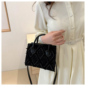Detail of black quilted fabric crossbody bag with white stitching and frayed edges
