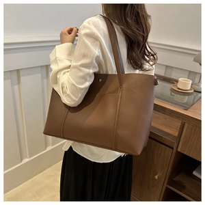 Detail of a large brown leather tote bag showing slim shoulder straps and fine vertical stitching