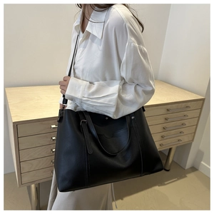 Model wearing a large black leather tote bag with adjustable strap in a bright interior
