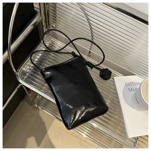 Détail de la pochette téléphone noire brillante avec boule tressée sur étagère métal