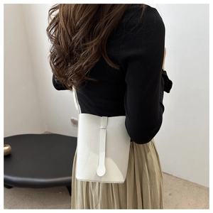 Detail of white litchi pattern bucket bag with minimalist strap worn by a model