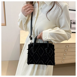 Detail of black denim quilted bag with fringe trim and leather handles on model