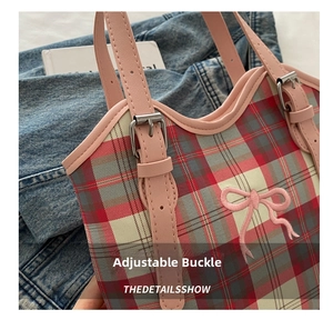 Détail de la bandoulière réglable en cuir rose avec boucle sur un sac à carreaux rouge