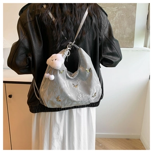 Sac hobo gris plissé avec détails papillons et breloque nuage porté par un mannequin