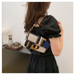 Détail d'un sac tricolore avec fermoir doré porté à l'épaule par un mannequin en scène