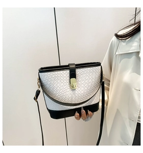 Detail of white woven texture leather bucket bag with black trim and gold rotating lock