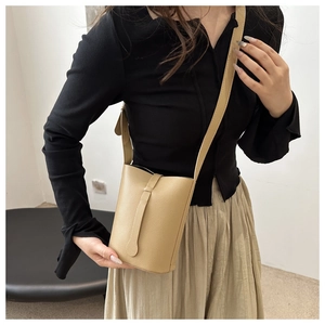 Close-up of beige lychee textured leather crossbody bucket bag with belt buckle detail