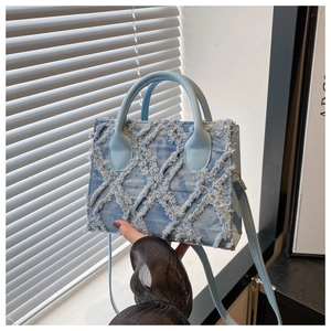 Detail of light blue denim crossbody bag with frayed edge diamond pattern and leather strap
