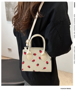 Detail of off-white corduroy mini tote bag with red strawberry embroidery on model
