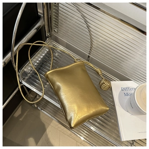 Détail d'un petit sac de téléphone doré brillant avec texture plissée et nœud décoratif