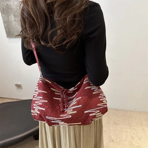 Deep red canvas hobo bag with colorful wavy embroidery and tassel drawstring detail