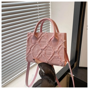 Detail of pink denim crossbody bag featuring frayed tassel texture and rhombic pattern