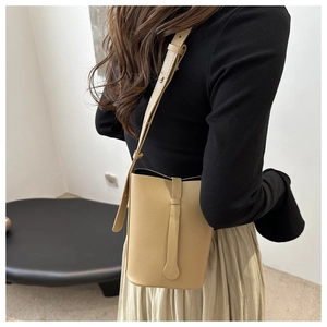 Detail of beige bucket bag showing litchi leather texture and adjustable shoulder strap