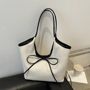 Minimalist black and white patchwork canvas tote bag with bow detail on a leather bench