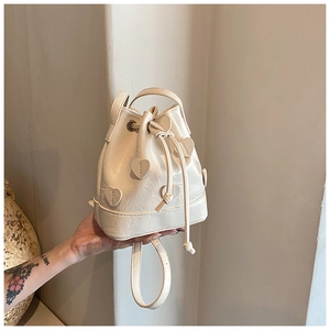 Detail of cream drawstring bucket bag featuring 3D heart patches and textured faux leather