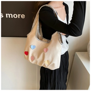 Detail der cremefarbenen Canvas-Tasche mit bunten Herz-Patches und silbernem Metallrand
