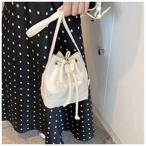 Detail of cream drawstring bucket bag with heart appliques and adjustable strap