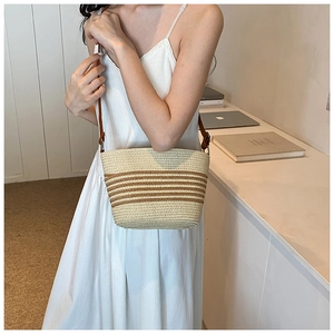 Detail of handwoven straw bucket bag with brown stripes and leather shoulder strap