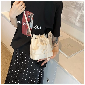 Detail of cream drawstring bucket bag featuring 3D heart appliqués and sleek leather strap