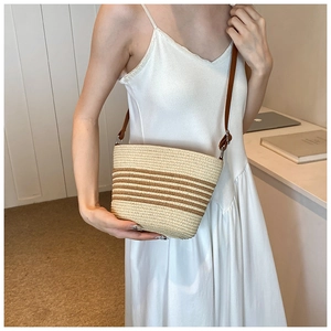 Detail of handwoven straw bag with dark brown stripes and slim leather crossbody strap