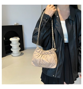 Dettaglio di una borsa a tracolla trapuntata beige con catena dorata su una modella