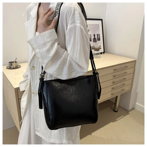 Detail of a black leather bucket bag with gold hardware worn as a crossbody bag