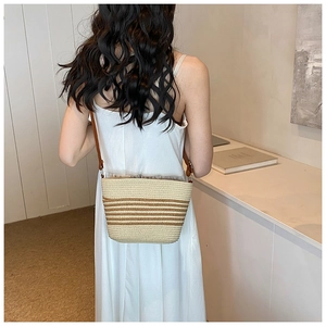 Detail of hand-woven straw tote with brown stripes and thin leather shoulder strap