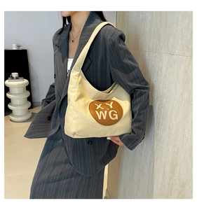 Detail of cream canvas tote bag featuring brown leather logo patch with embossed lettering