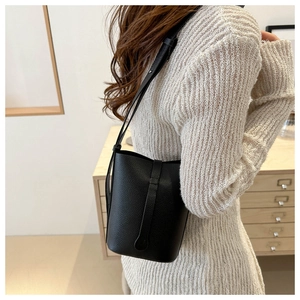 Detail of black pebbled leather bucket bag with slim shoulder strap on female model