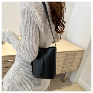 Detail of black pebbled leather bucket bag with long flap accent and slim shoulder strap